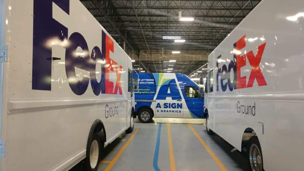A Sign & Graphics truck with two FedEx trucks