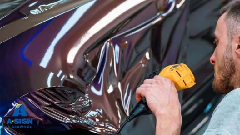 A technician uses a heat gun to apply a reflective vinyl wrap to the side of a vehicle, smoothing out air bubbles and creases. The process is part of a detailed vehicle wrap installation.